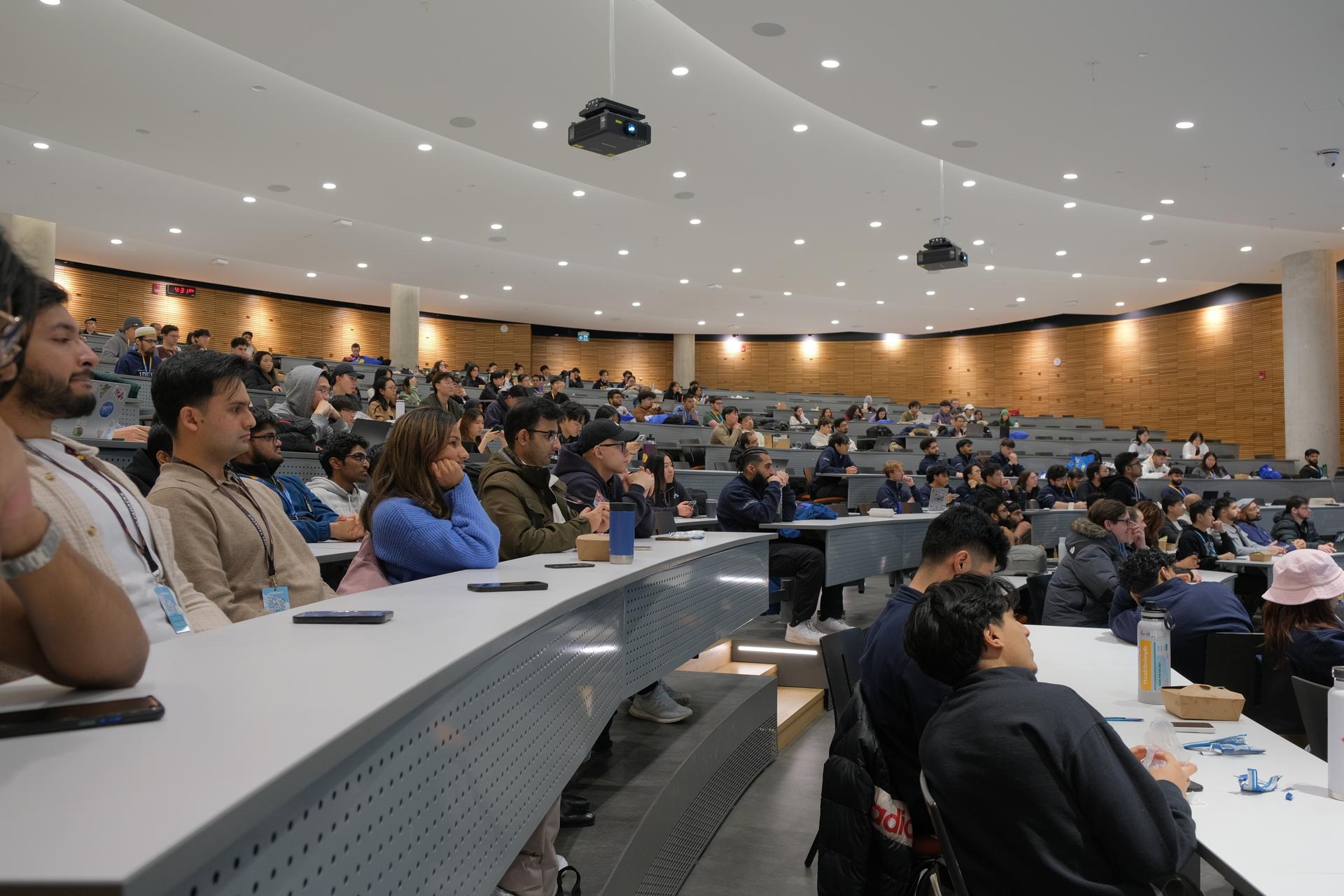 A wide view of a packed lecture hall with rows of seated students, eager for DeltaHacks to start.